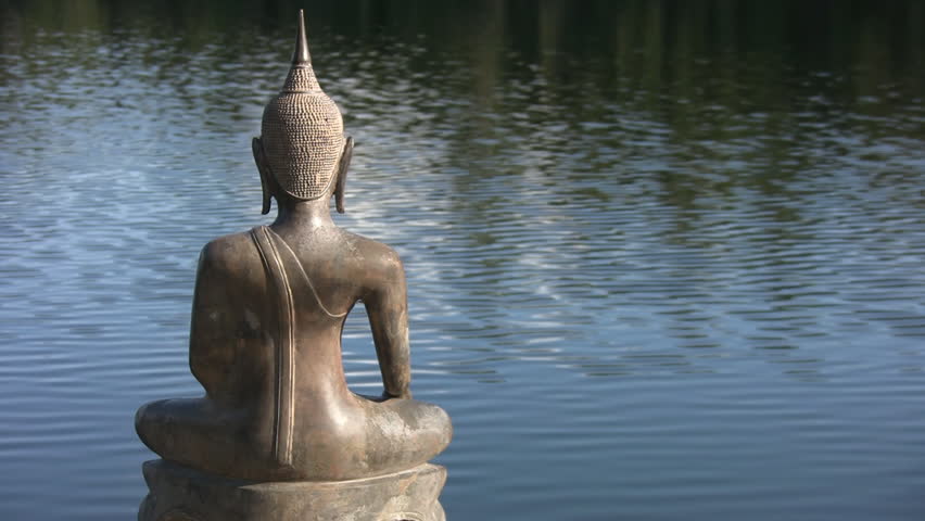 Buddha by the lake.  A seated statue of Buddha sits by the lake. Space for text on right side. 
