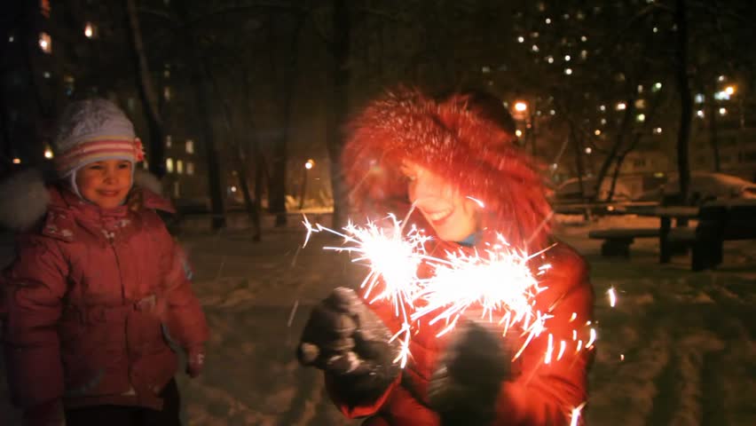 young woman with sparkler, near little girl, night outdoor 