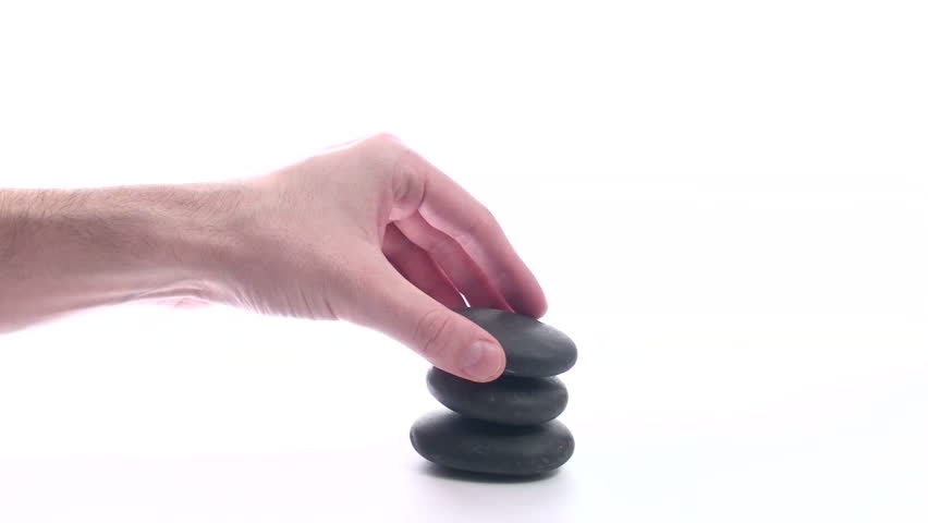 Hand stacks Zen rocks against white background wide shot