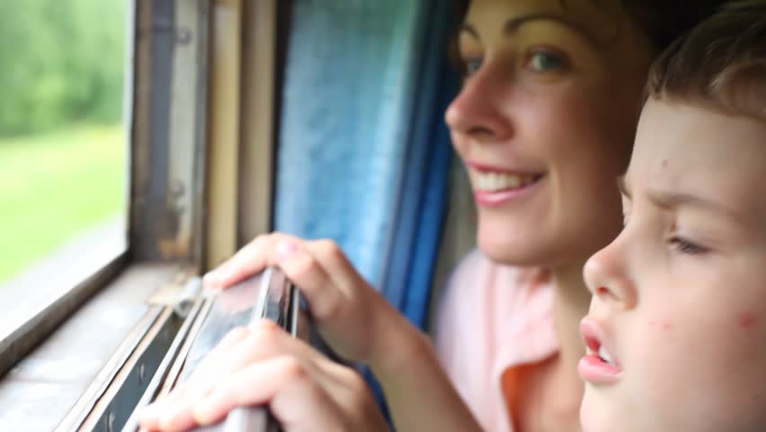 young woman and boy looking on nature from moving railway carriage 
