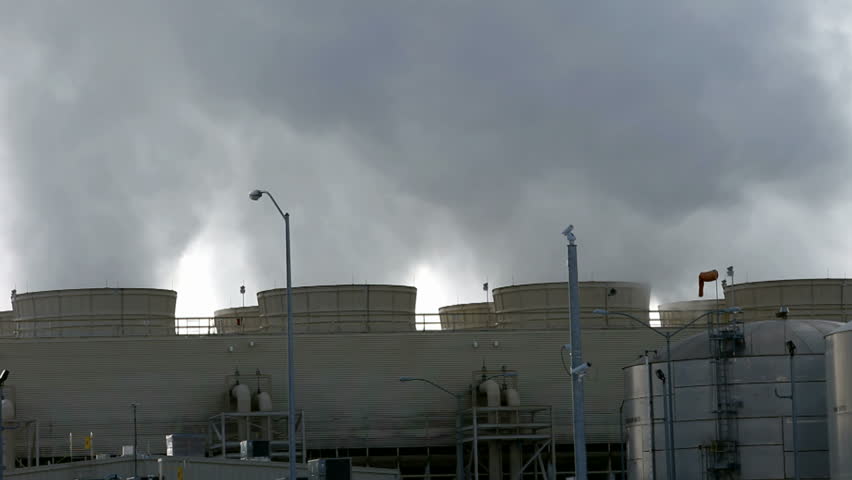 Pollution and steam spewing from cooling towers and smoke stacks of a natural gas electrical generating power plant. White and gray smoke with a while background sky.