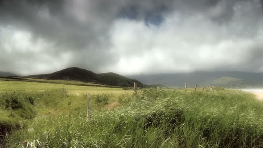 Irish valley with grasses blowing in the wind.  It is a cloudy day with lots of sun.