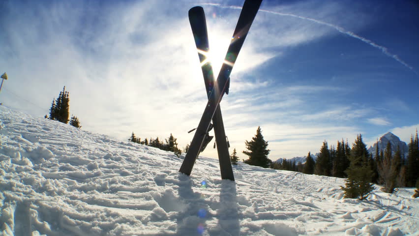 Crossed carver downhill skis & poles standing in fresh clean snow high in scenic mountain landscape
