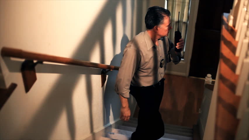Startled by a noise, a detective stops talking on his radio, draws his gun, and walks cautiously up the staircase to investigate. Color enhanced for affect.