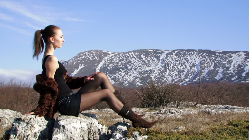 A woman sitting on a rock. Beautiful girl fashion model sitting on a rock against the beautiful natural scenery.