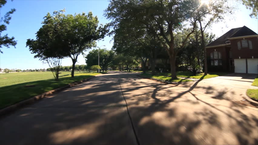 Hood view from a vehicle as it drives down a sunny, tree lined, street and pulls into a driveway as the garage door opens.