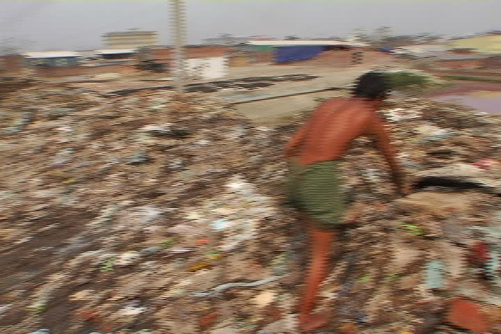 A young man digs through a mountain of trash near the shores of a toxic pond, in a Bangladesh slum.