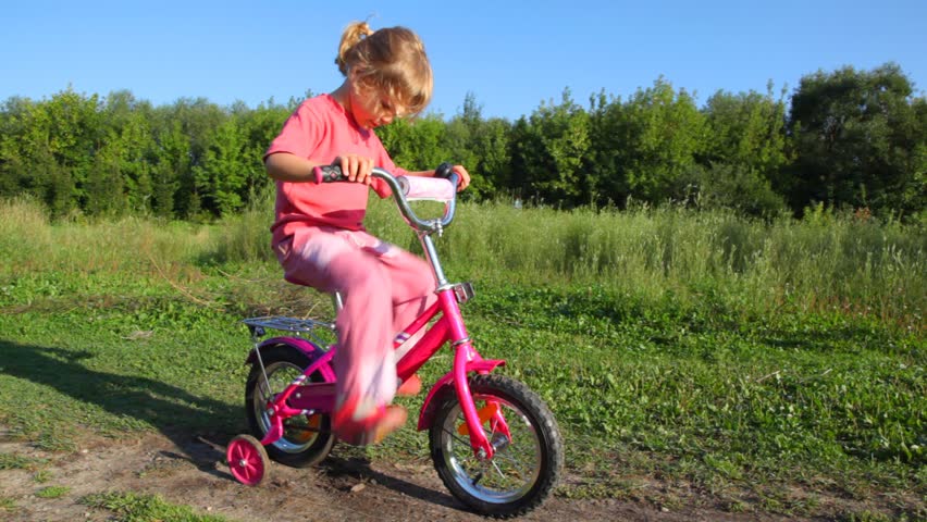 little girl treadling stopped bicycle, boy rides to her and pushes 