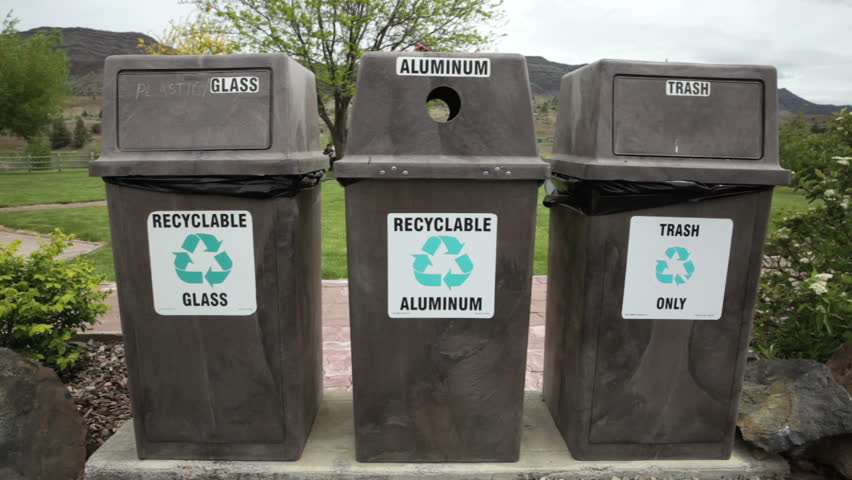 Three recycling bins and trash cans in a park, dolly shot