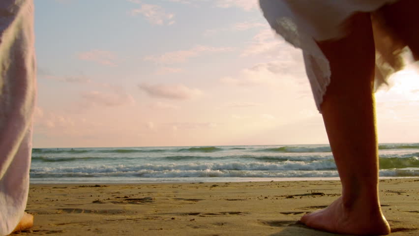 Older couple holds hands and walks into the sunset together. 