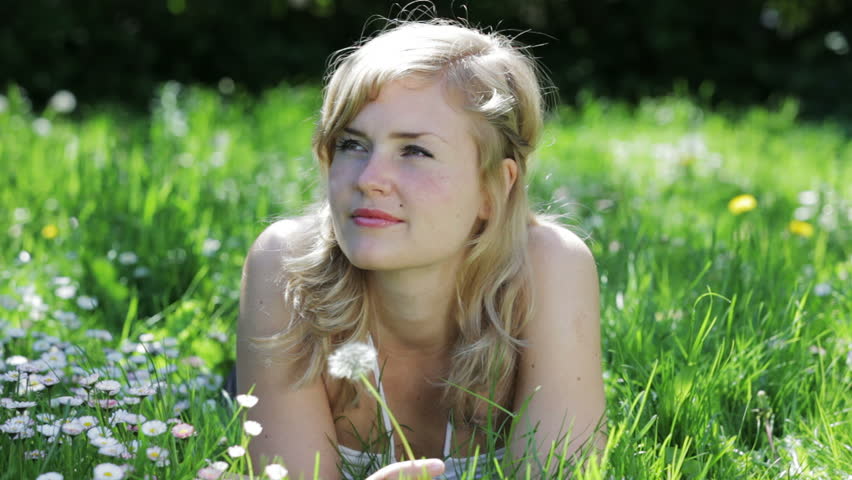 A young blond woman blowing on a dandelion