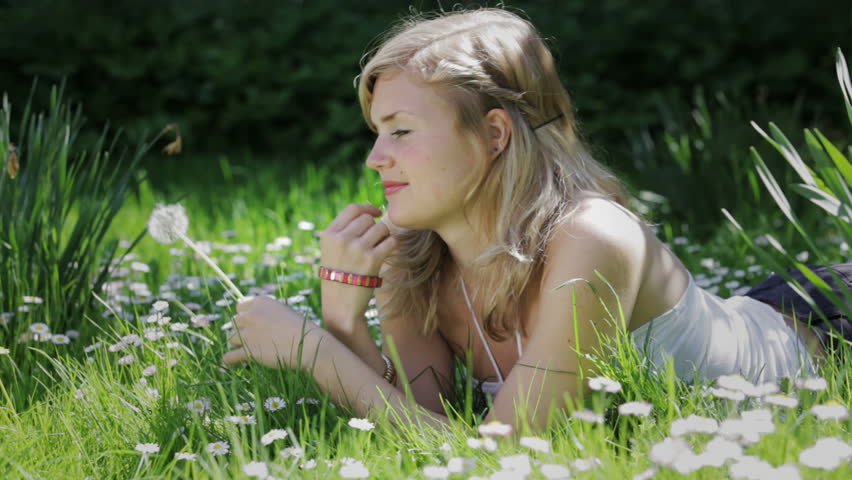 A young blond woman blowing on a dandelion