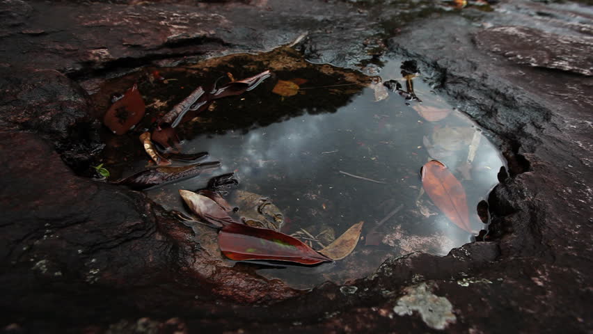 Close up of a hand playing with rainwater which is collected in a whole of a dark red rock