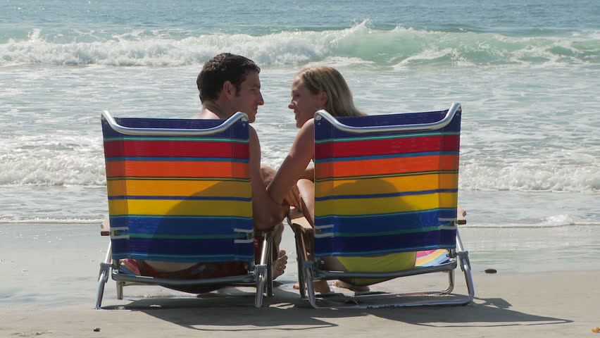 Young couple sitting in lounge chairs by ocean and kissing