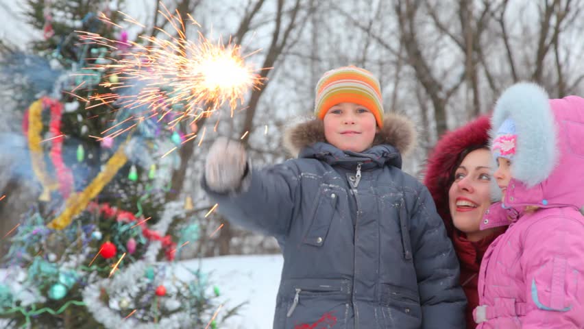 happy family of three with sparkler against decorated Christmas tree outdoor