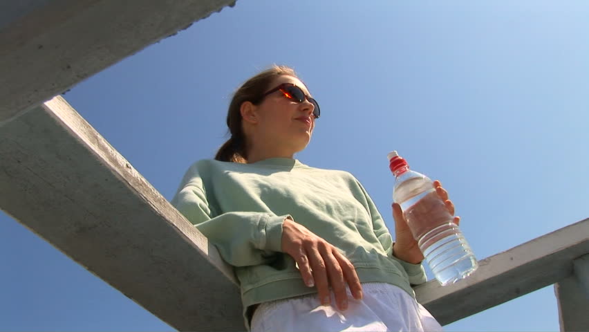 Young woman leaning on railing outside drinking water