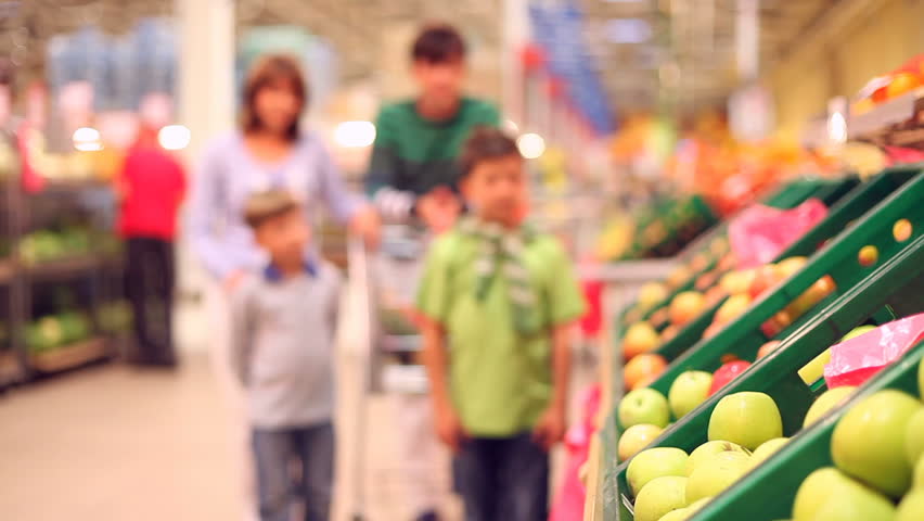Two boys taking oranges from the shelf and putting them into the shopping trolley of their parents 