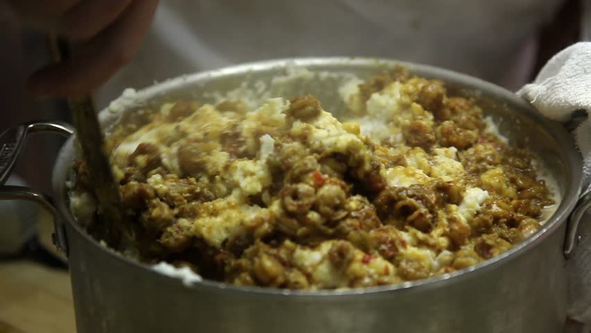 Hands of a male chef creating a cajun gourmet dish by stirring tasty seasonings and steaming ingredients incl. crawfish tails into a large pot of potatoes, using interesting rhythm and motion. 