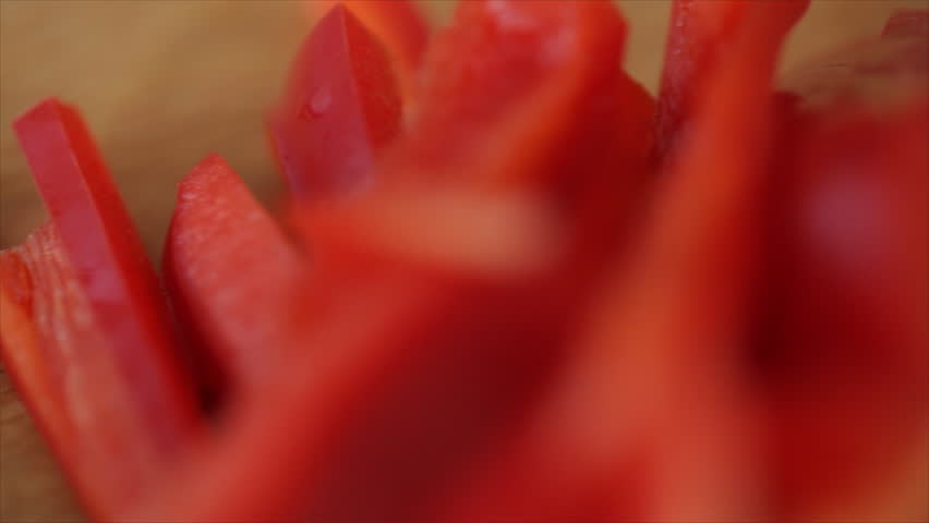 The camera pans past sliced red bell pepper and shallots to focus on a woman slicing a purple onion.