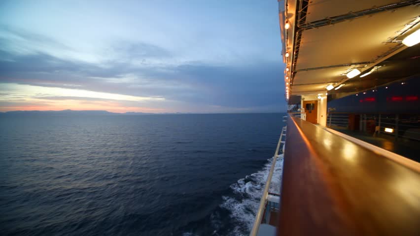 woman walks on illuminated deck of cruise ship moving in evening sea