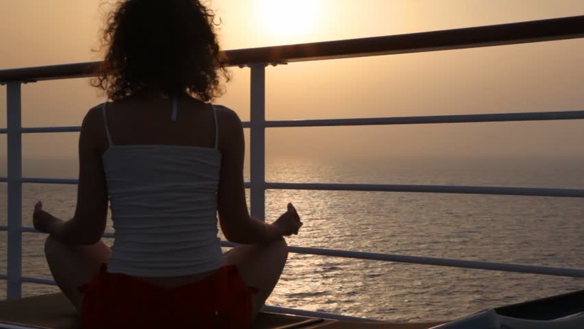 woman sits in pose of lotus on deckchair on deck of cruise ship in evening sea