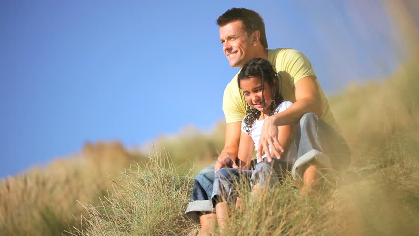 Young caucasian father with his mixed race daughter having fun together in the sand dunes by the coast
