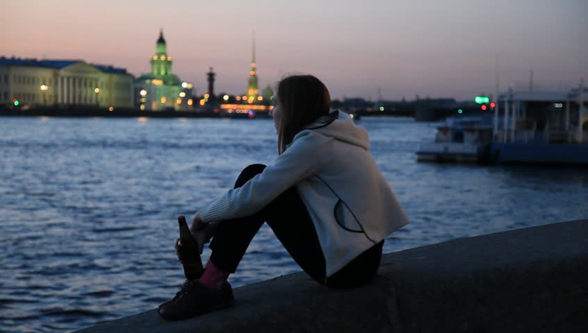 Smiling girl with bottle beer on the waterfront at night, St. Petersburg, Russia