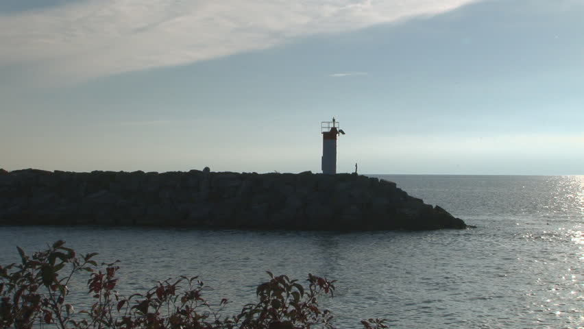 Back-lit wide angle shot of break-wall and harbor beacon at sunrise