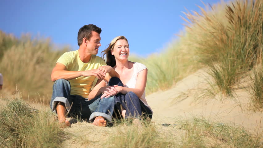 Attractive young caucasian family enjoying time together & the children having fun playing in sand dunes