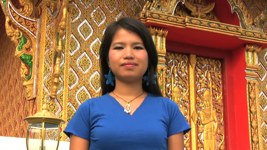 A pretty Thai girl demonstrates a typical Thai greeting called the "wai" as she stands in front of a Buddhist temple in Bangkok, Thailand.
