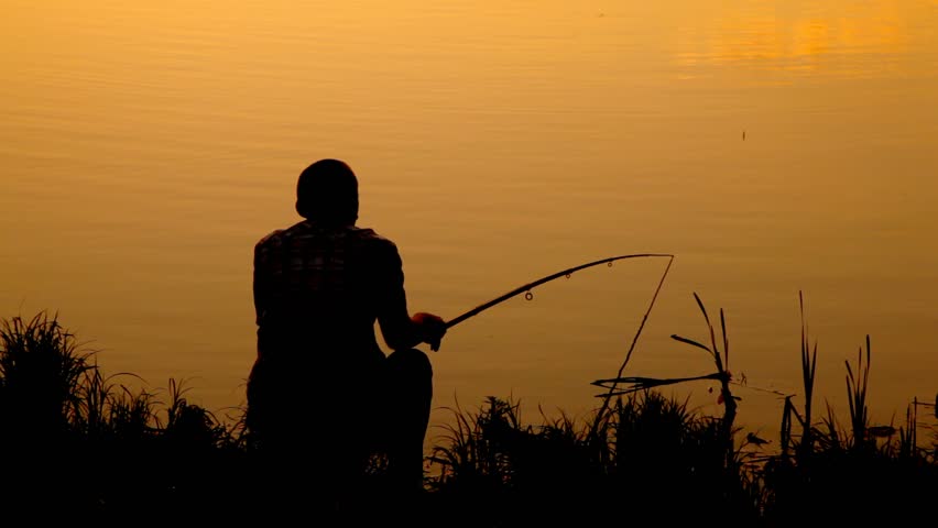 back view of man sitting near water and fishing during sunset