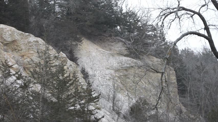 Wintry view of a scenic river in Minnesota during a snowfall. Camera tilts down from a hillside to the river.
