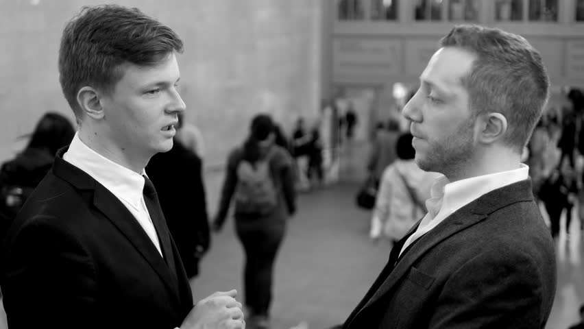 Black And White Background Of Two Young Business Professionals Having A Conversation In Crowded