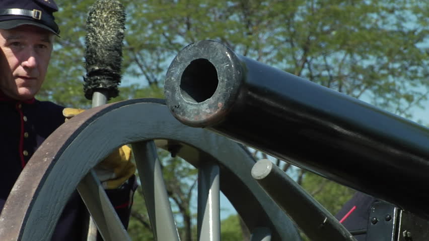 American Civil War era cannon fires in flame and smoke as crew member covers ears.