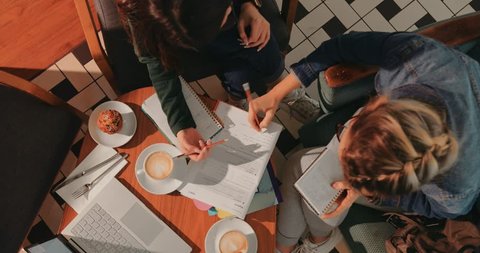 Top view of female college students with books and notebooks studying together at coffee shop