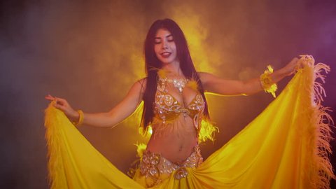 Exotic Naked Beach - Seductive sexy traditional oriental belly dancer girl dancing on yellow  neon smoke background. woman in exotic costume with feathers sexually moves  her semi-nude body.