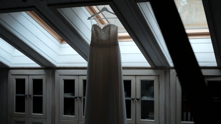 The Wedding Dress Hangs Against A Dormer Window