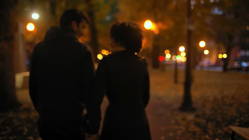 A Cute Young Couple Walk Through A City At Night Together. Medium Shot ...